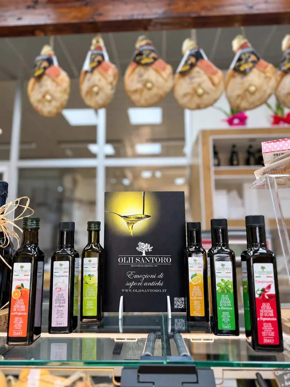 Il banco del punto vendita con l'olio e i prosciutti appesi